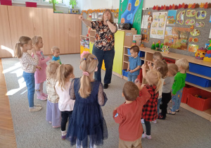 Dzieci stoją w kole i tańczą naśladując gesty pokazywane rzes panią prowadzącą warsztaty.