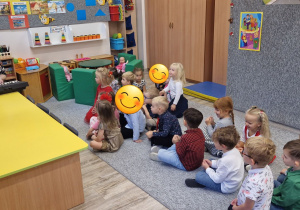 Dzieci siedzą na dywanie i śpiewają nowo poznaną piosenkę do akmpaniamentu keyboardu.