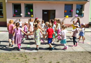 Dzieci tańczą w kółeczku na dziedzińcu przedszkola