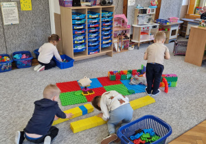 Dzieci siedzą a dywanie i budują z kolorowych klocków.