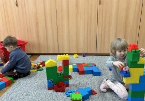 Dziewczynka i chłopiec budują z dużych klocków.