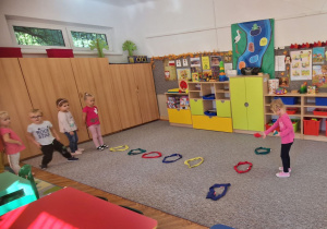 Dzieci przeskakują obunóż przez kolorowe szarfy.