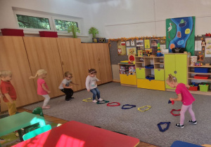 Dzieci przeskakują obunóż przez kolorowe szarfy.
