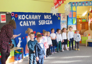 Dzieci z grupy Żabek, ustawione na tle napisu "Kochamy Was całym sercem", prezentują program artystyczny dla Babci i Dziadka.