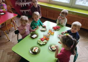 Dzieci z grupy Żabek siedzą przy zielonym stole i prezentują samodzielnie ozdobione kanapki.