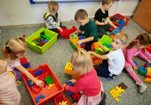 Dzieci bawią się na dywanie budując z klocków.