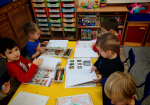 Dzieci siedzą przy stołach i podejmują próby rozwiązywania zadań w kartach pracy.