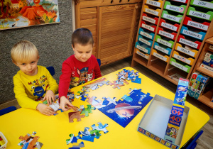 Chłopcy siedzą przy stole i układają puzzle.