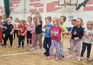 Dzieci ustawione na sali gimnastycznej tańczą.