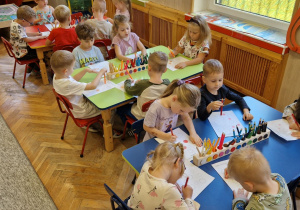 Dzieci siedząc przy kolorowych stołach wykonują zadania matematyczne z kropkami w roli głównej.