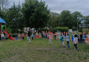 Dzieci tańczą z panią w ogrodzie przedszkolnym.