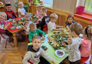 Dzieci przyklejają liście do papierowego talerzyka wyklejonego taśmą klejącą.