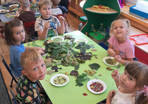 Dzieci przyklejają liście do papierowego talerzyka wyklejonego taśmą klejącą.
