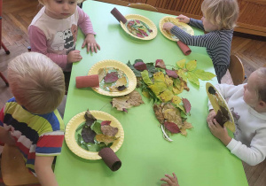 Dzieci przyklejają liście do papierowego talerzyka wyklejonego taśmą klejącą.