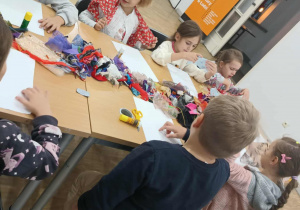 Dzieci siedzą przy stole i wycinają materiałowe elementy do portretu