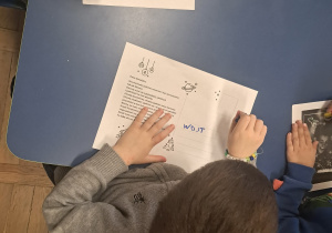 Dzieci siedzą przy niebieskim stole i podpisują listy.