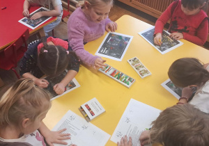 Dzieci siedzą przy żółtym stole i przygotowują, kolorują list.