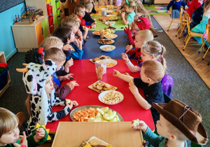 Dzieci siedzą przy stołach i delektują się słodkościami.