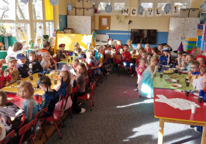 Dzieci siedzą przy stołach i delektują się słodkościami.