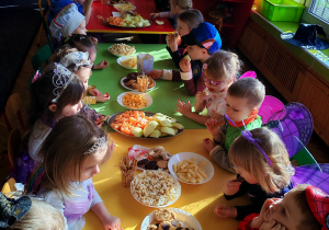 Dzieci siedzą przy stołach i delektują się słodkościami.