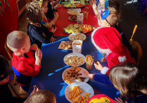 Dzieci siedzą przy stołach i delektują się słodkościami.