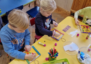 Dzieci siedzą przy żółtym stole i ozdabiają ramki.