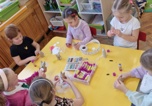 Dzieci siedzą przy żółtym stole i tworzą koty.