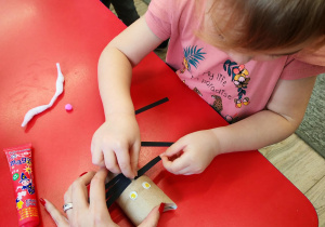 Dziewczynka dokleja wąsy z pasków czarnego papieru.