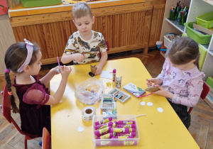 Dzieci siedzą przy żółtym stole i tworzą koty.