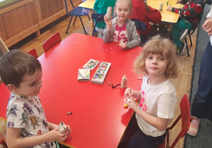 Dzieci siedzą przy czerwonym stole i tworzą koty.