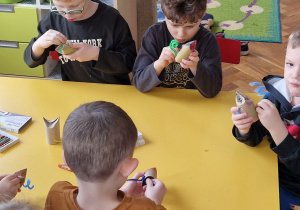 Dzieci siedzą przy żółtym stole i tworzą koty.