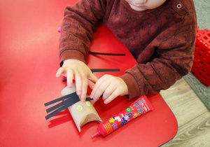 Chłopiec dokleja wąsy z pasków czarnego papieru.