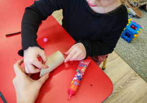 Dziewczynka dokleja wąsy z pasków czarnego papieru.