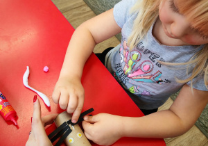 Dziewczynka dokleja wąsy z pasków czarnego papieru.