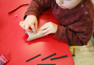 Chłopiec dokleja wąsy z pasków czarnego papieru.