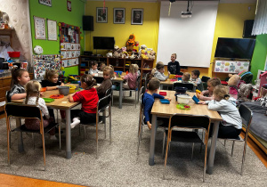Dzieci siedzą przy stolikach i czekają na rozpoczęcie zajęć.